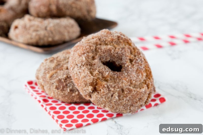 Freshly fried apple cider donuts stacked on a white napkin, ready to be coated.