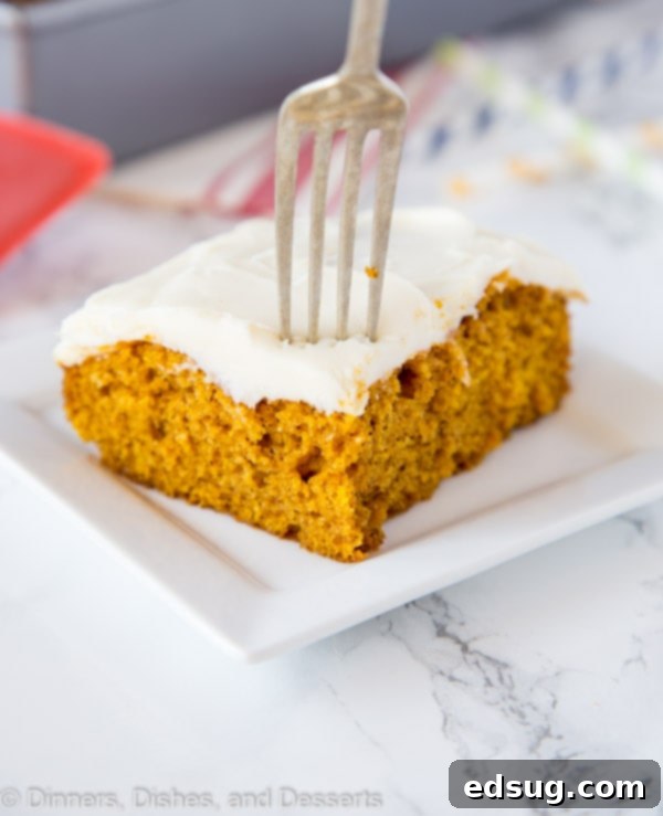 A perfectly sliced piece of pumpkin cake on a white plate, served with a fork, showing the fluffy texture and creamy frosting.