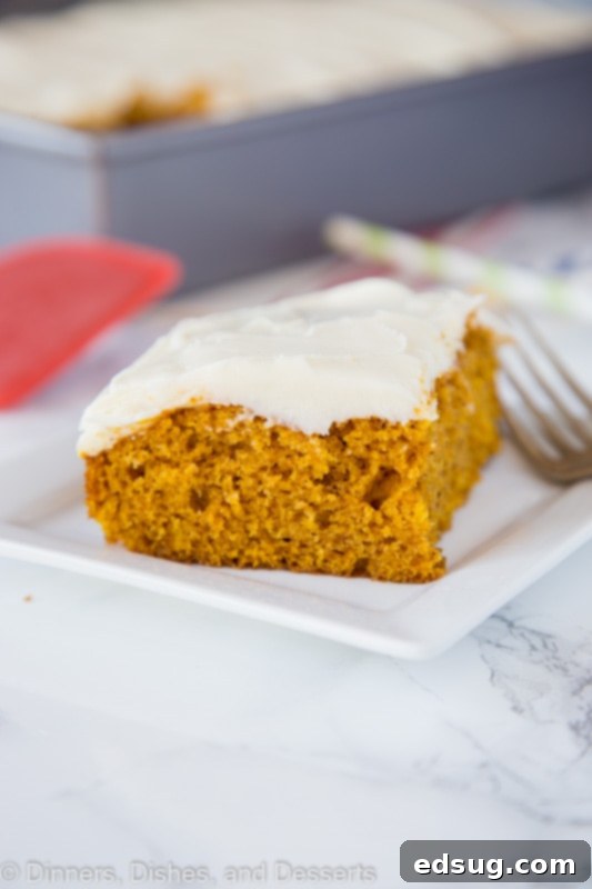 A delightful slice of pumpkin cake topped with a generous swirl of cream cheese frosting on a pristine white plate.