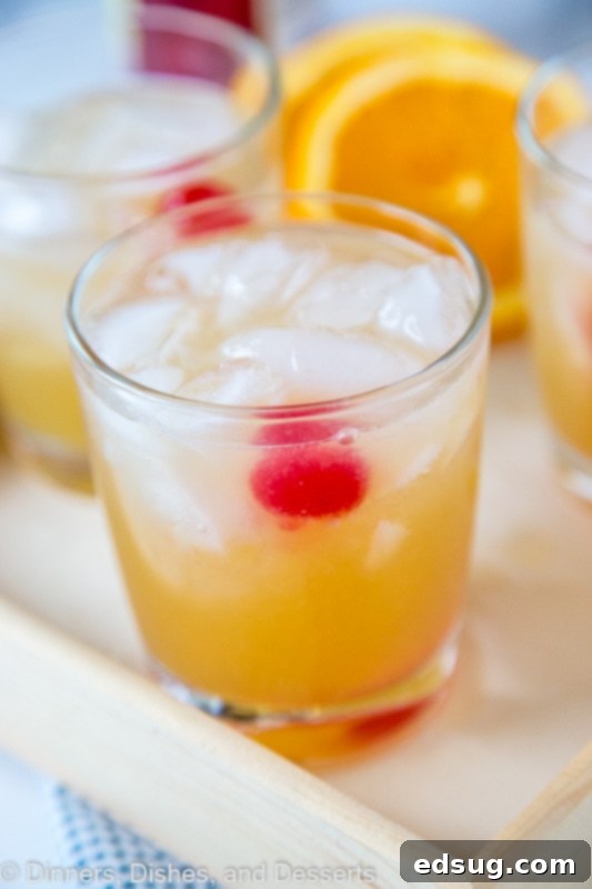 A perfectly chilled glass of homemade Whiskey Sour, garnished with a vibrant maraschino cherry and a slice of orange, sitting on a rustic wooden tray, ready to be enjoyed.