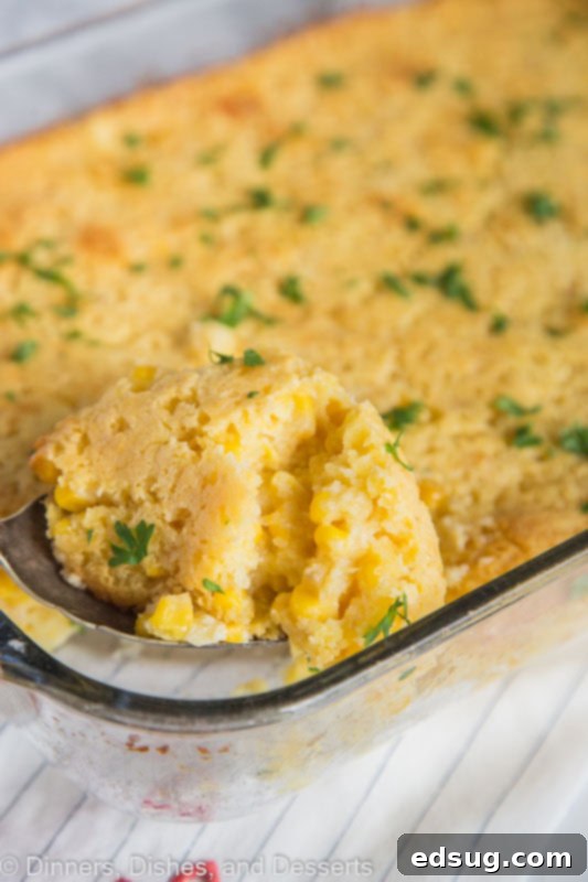 A serving spoon lifting a spoonful of creamy corn casserole from a baking dish, highlighting its rich texture and golden crust.