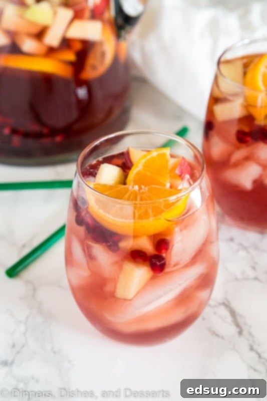 Festive Christmas Sangria 3 A refreshing close-up of Christmas Sangria in a glass, featuring white wine, vibrant pomegranate seeds, and citrus slices, ready to be enjoyed.