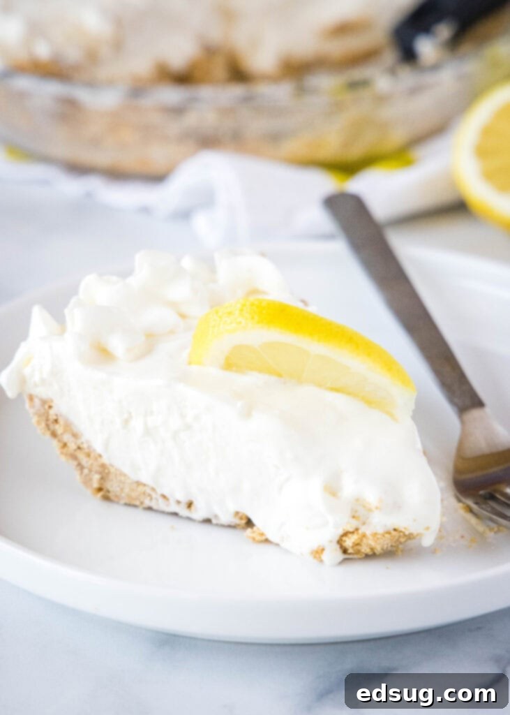 slice of creamy lemonade pie on a white plate with a fork and lemon garnish