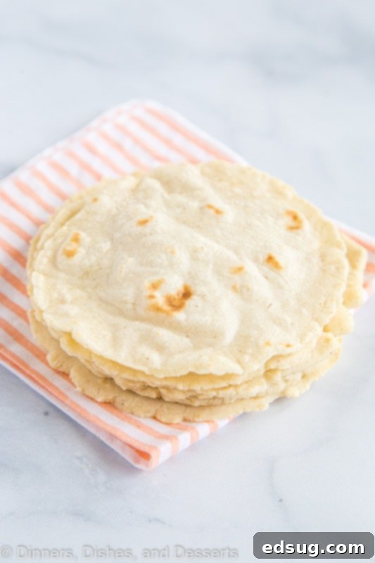 A stack of perfectly cooked homemade corn tortillas, featuring golden-brown spots and a soft, pliable texture.