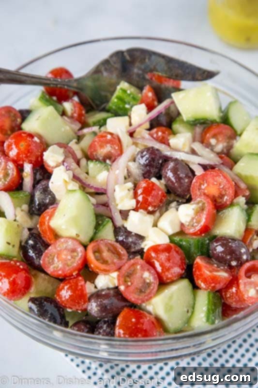 Greek Salad tossed together in serving bowl, showcasing fresh cucumbers, tomatoes, red onions, olives, and feta cheese