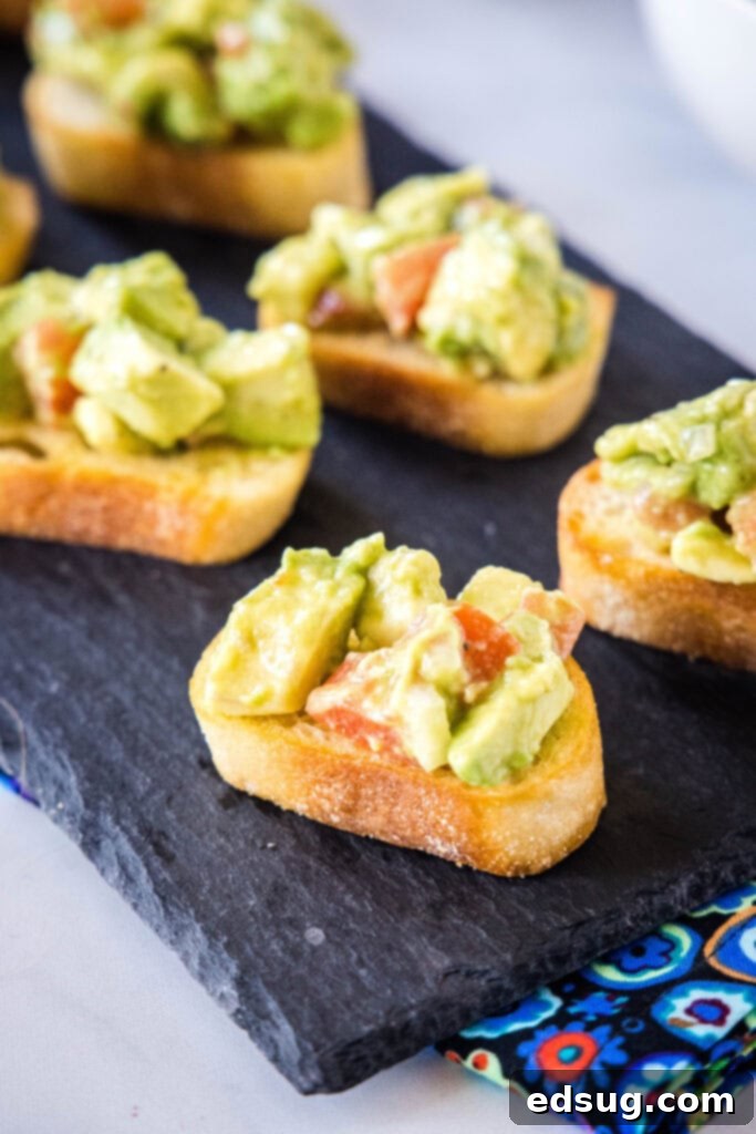 A vibrant serving tray of freshly prepared avocado bruschetta, with each toast topped with a generous portion of avocado and tomato mixture.
