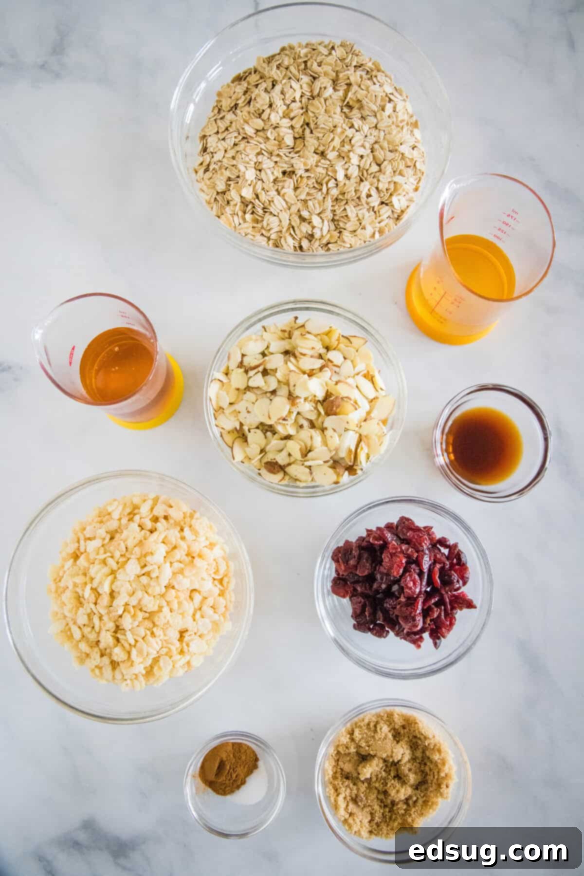 Classic Vanilla Granola 2 Ingredients for homemade vanilla almond granola, including oats, almonds, cinnamon, and vanilla extract, laid out on a white surface