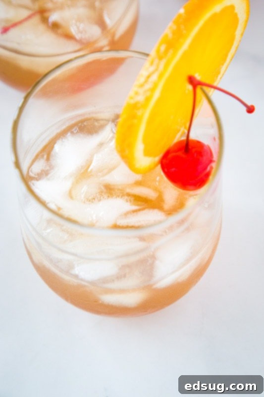 Classic Amaretto Sour Recipe 3 Amaretto sour recipe is super easy and delicious, showing a close-up of the cocktail in a glass with ice, an orange slice, and a maraschino cherry.