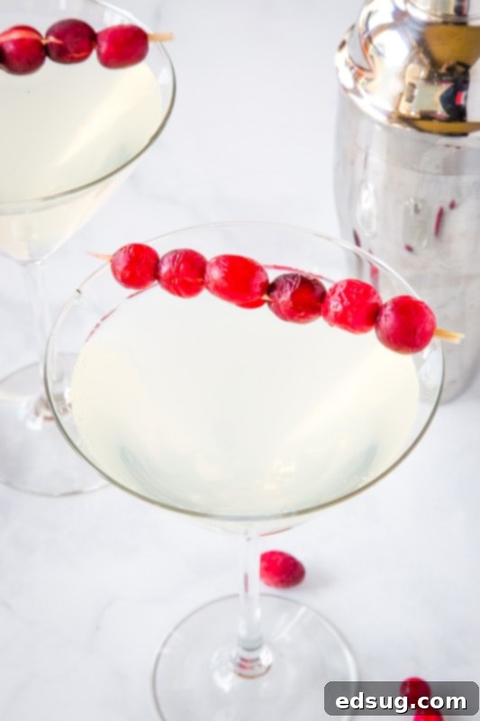 Elegant Winter White Cosmo cocktail in a martini glass, garnished with fresh cranberries, perfect for a sophisticated holiday party.