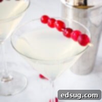 A stunning Winter White Cosmo, adorned with fresh cranberries, in a martini glass. Fruity, tart, and perfect for holiday parties!