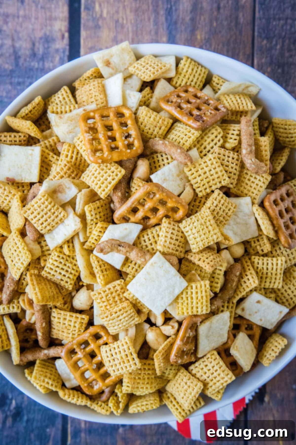 Zesty Taco Crunch 2 An overhead view of a rustic wooden bowl filled with a fresh batch of Taco Snack Mix, showcasing the golden-brown crunch of cereal, nuts, and seasoned tortillas.