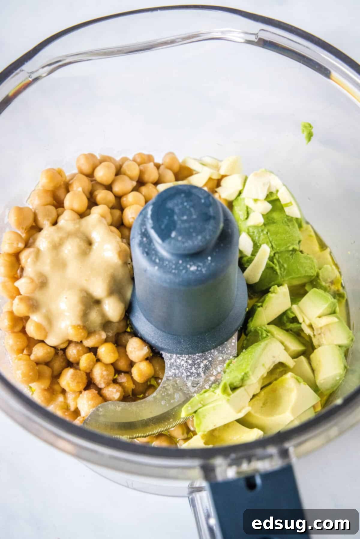 All avocado hummus ingredients in a food processor, ready to be blended into a smooth dip.