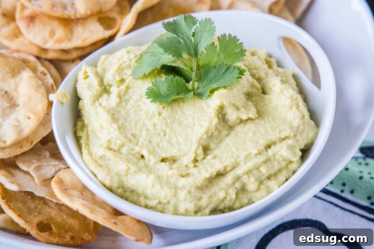A large bowl of avocado hummus with various dippers like pita bread, crackers, and vegetable sticks.