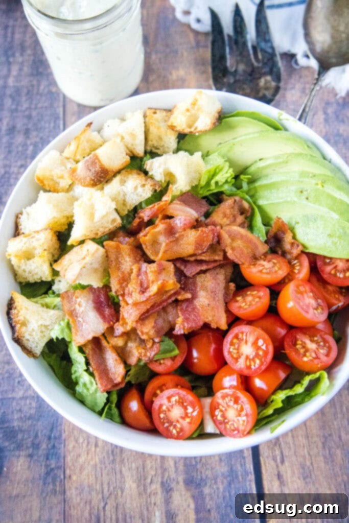 Looking down on a bowl of BLT Salad, featuring crispy bacon, vibrant lettuce, red tomatoes, golden croutons, and creamy avocado, ready to be tossed with dressing.