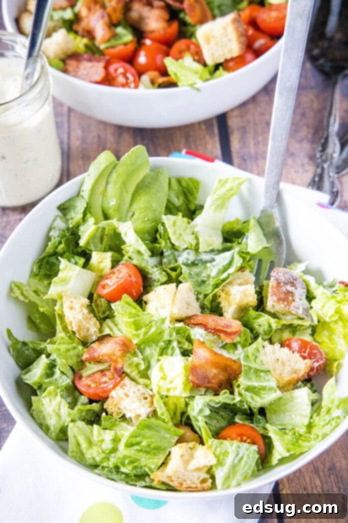 A vibrant BLT salad, perfectly tossed in a large bowl, with a fork ready to serve. Shows off the rich colors of bacon, lettuce, tomatoes, and croutons.