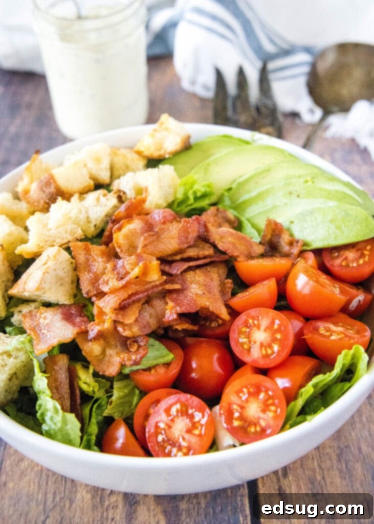 Arrangement of fresh BLT salad ingredients in separate sections of a bowl, showcasing vibrant lettuce, red tomatoes, crispy bacon, and creamy avocado before mixing.