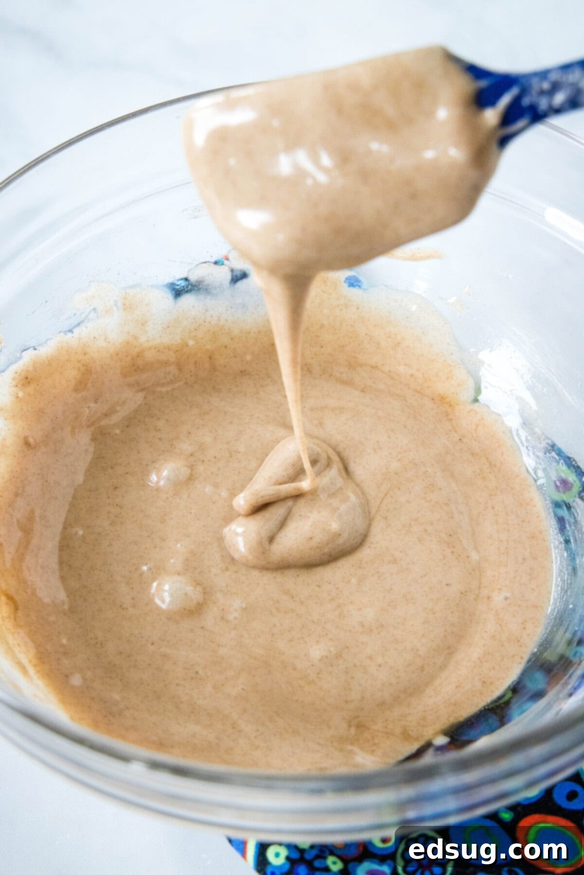 Spiced Apple Cider Cookies 3 A spoon drizzling apple cider glaze into a bowl.