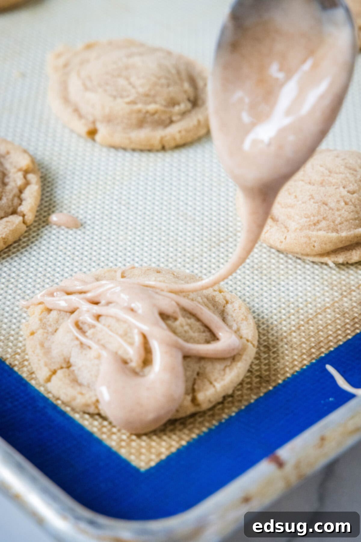 Spiced Apple Cider Cookies 4 A spoon is used to drizzle glaze over baked apple cider cookies on a lined baking sheet.