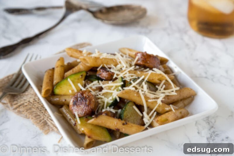 A close-up shot of balsamic pasta showing perfectly cooked chicken sausage, vibrant zucchini, and red onion coated in the glossy balsamic sauce on a white plate, ready to be enjoyed.