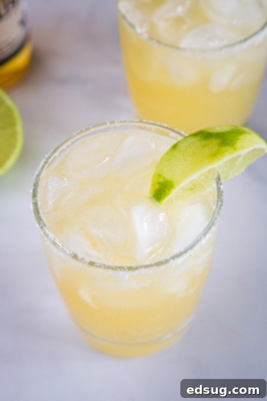 The Ultimate Beer-Garita 4 A close-up of a refreshing Beer Margarita in a salted glass, garnished with a lime wedge, with a blurred background suggesting a lively setting.