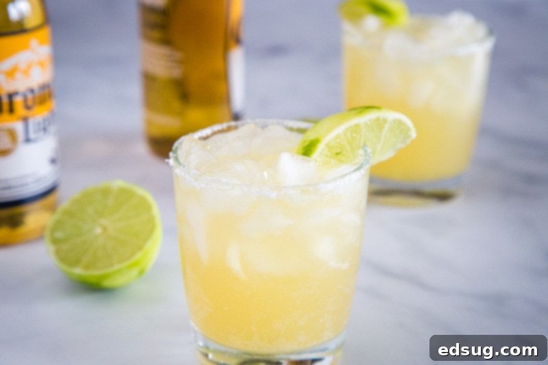 The Ultimate Beer-Garita 5 Four glasses of Beer Margaritas garnished with lime wedges, arranged on a wooden surface, ready for a party.