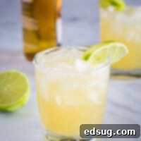 A glass of beer margarita garnished with lime, with a beer bottle in the background, signaling a refreshing drink.