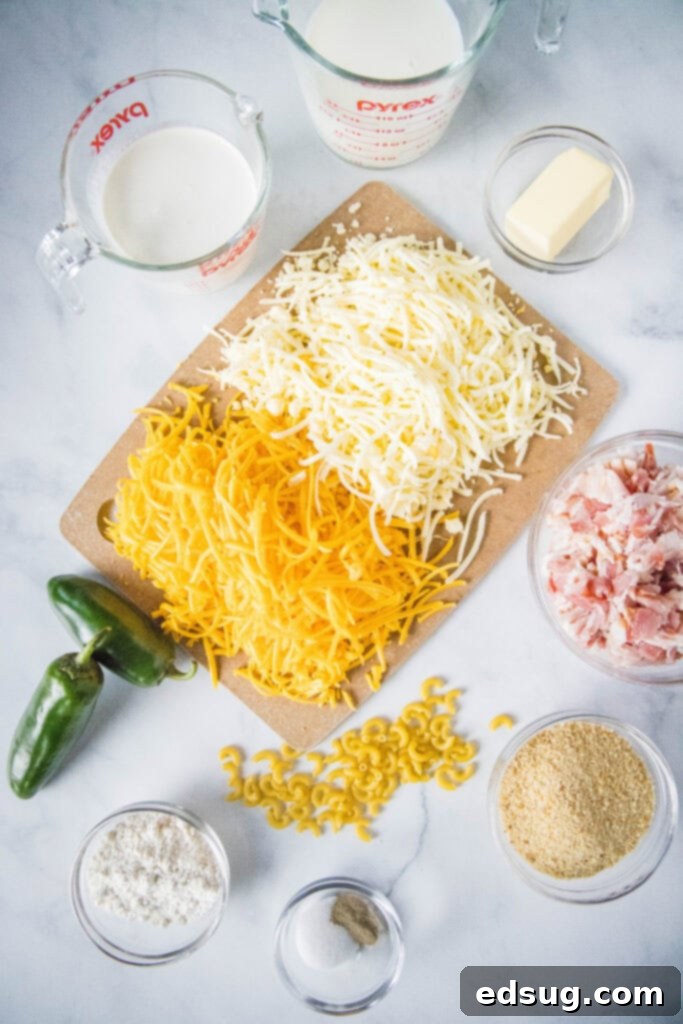 A selection of fresh ingredients for making Jalapeño Popper Mac and Cheese laid out on a wooden board, including block cheeses, pasta, bacon, and fresh jalapeños.