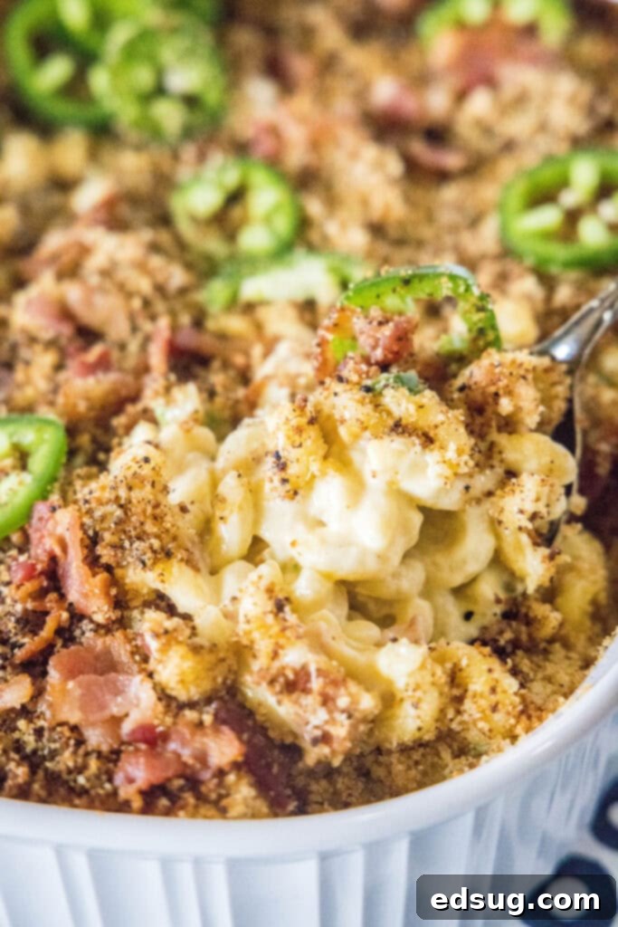 A serving spoon lifting a portion of hot, bubbly Jalapeño Popper Mac and Cheese from a baking dish, showcasing its creamy texture and crispy topping.