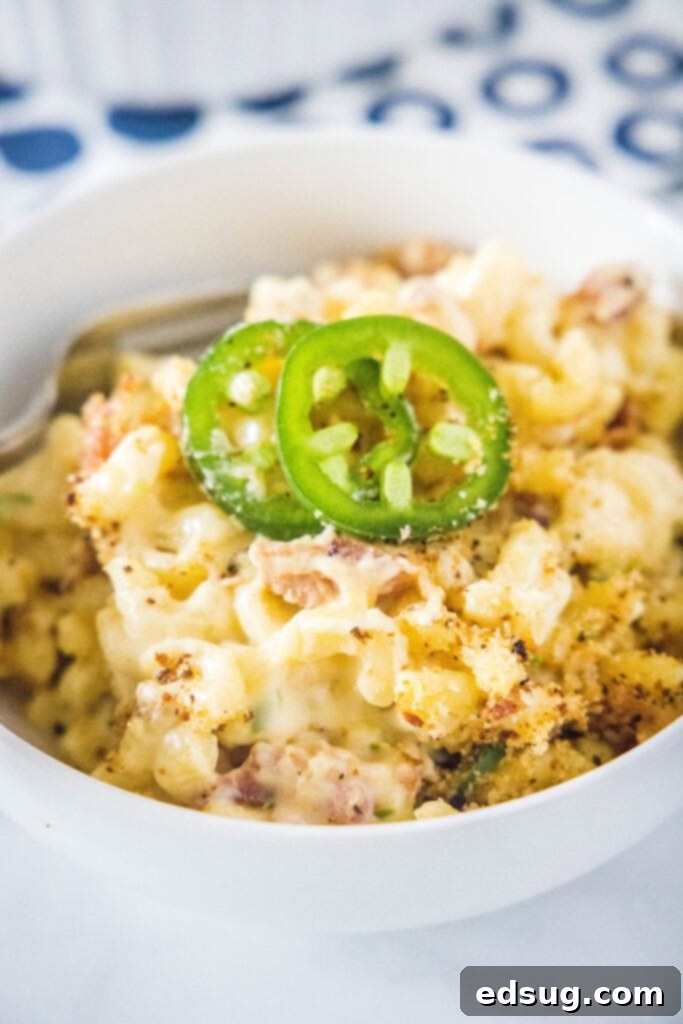 A single serving bowl of creamy Jalapeño Popper Mac and Cheese, garnished with fresh jalapeño slices and crispy bacon crumbles on top.