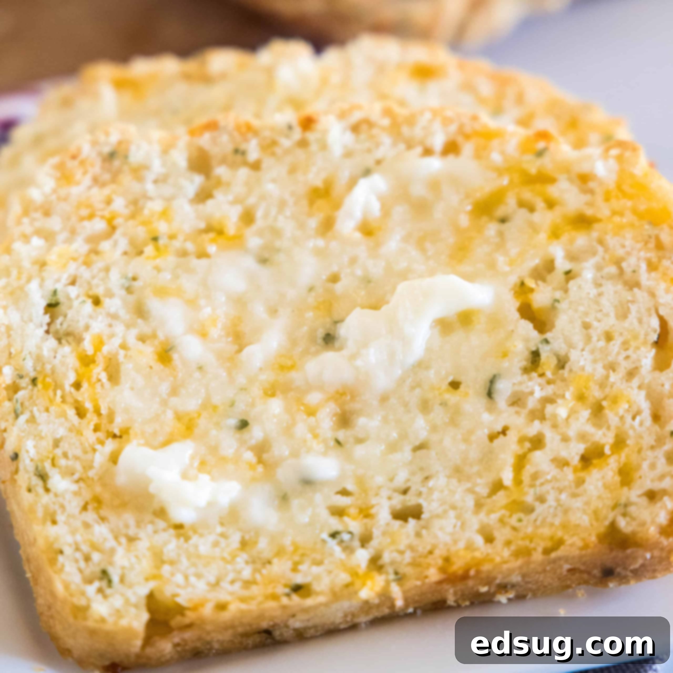 Close up of a slice of cheesy quick bread spread with butter.