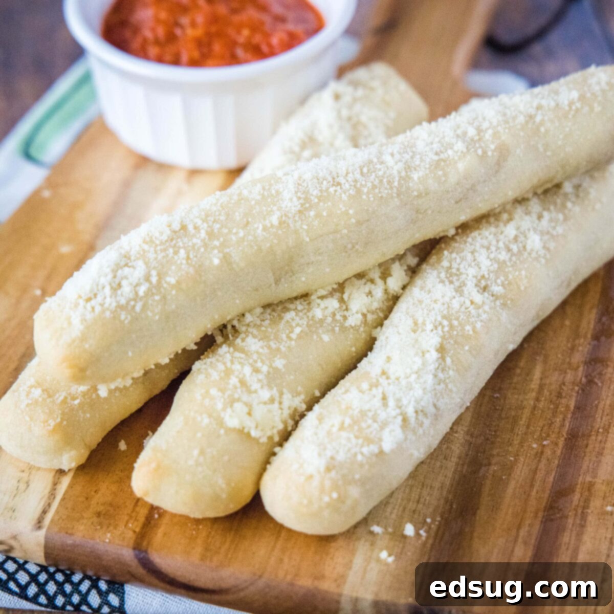 Four irresistible breadsticks on a wooden cutting board, accompanied by a ramekin of marinara sauce, resembling Little Caesars Crazy Bread.