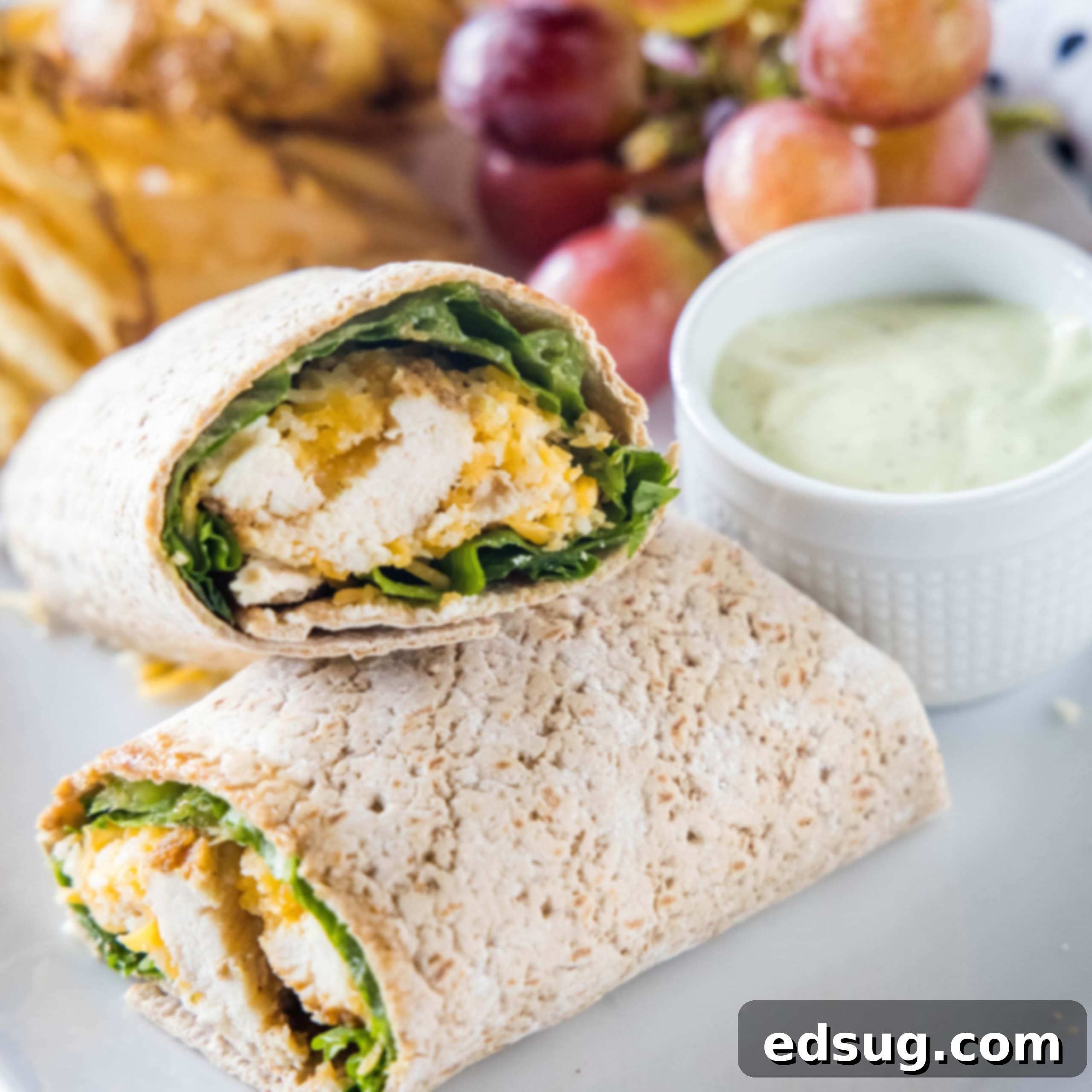 Two halves of a Chick-Fil-A Cool Wrap beautifully arranged on a plate with a side of dipping sauce, fresh grapes, and crispy potato chips.