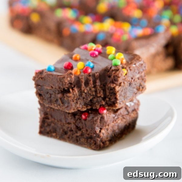 Decadent Cosmic Brownies, a homemade twist on the classic childhood treat, topped with chocolate fudge frosting and colorful rainbow sprinkles.