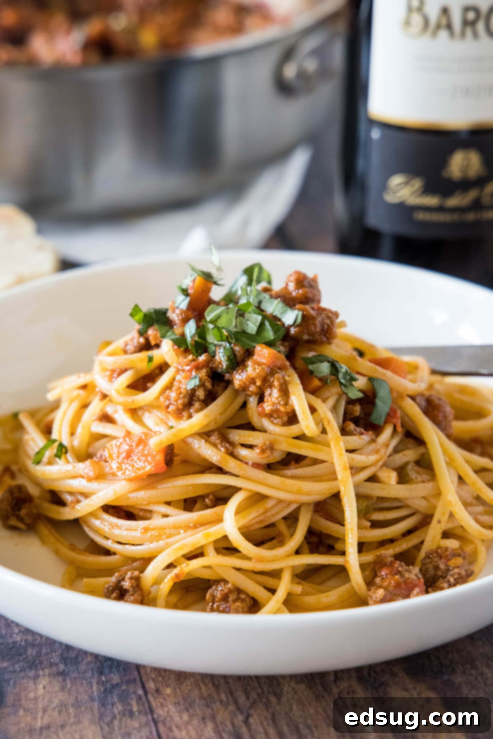 A generous serving of authentic Italian beef ragu with spaghetti in a pristine white bowl, garnished with fresh basil.