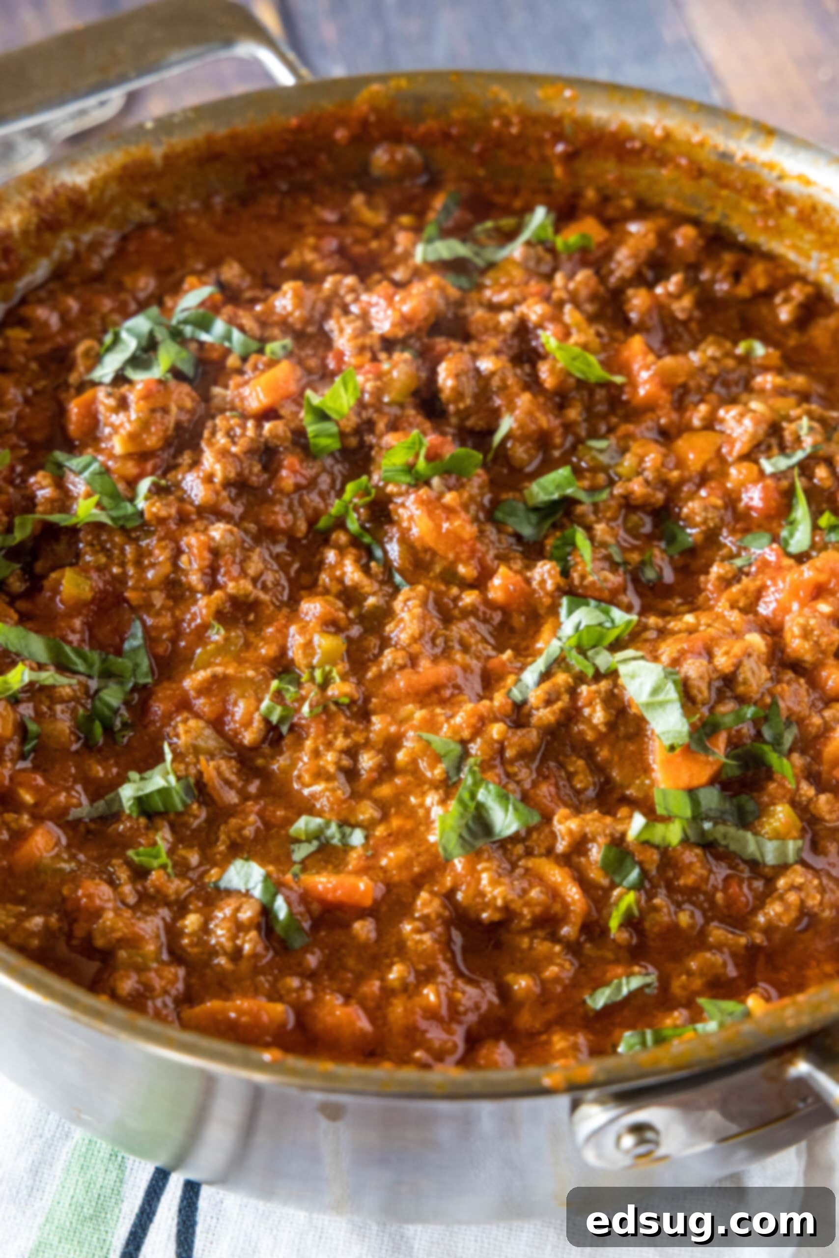 A large, deep skillet brimming with hearty beef ragu, beautifully garnished with fresh basil leaves, ready to be enjoyed.