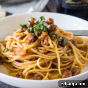Beef ragu served with spaghetti in a white bowl.