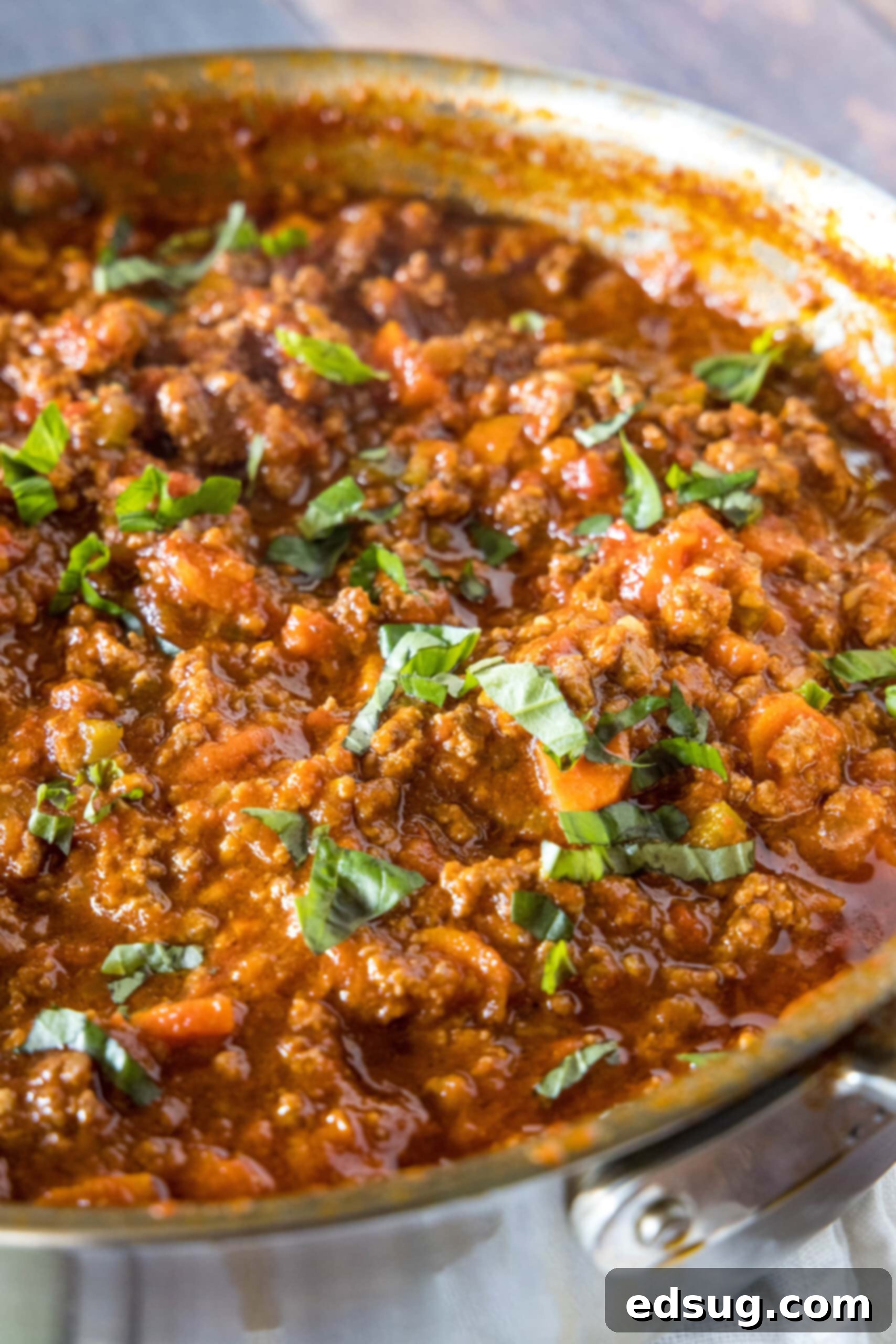 A large, deep skillet filled with bubbling beef ragu, garnished with freshly chopped basil leaves, ready to be served.