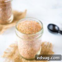 A jar of the Best Dry Rub For Ribs spices on a table, with delicious ribs in the background.