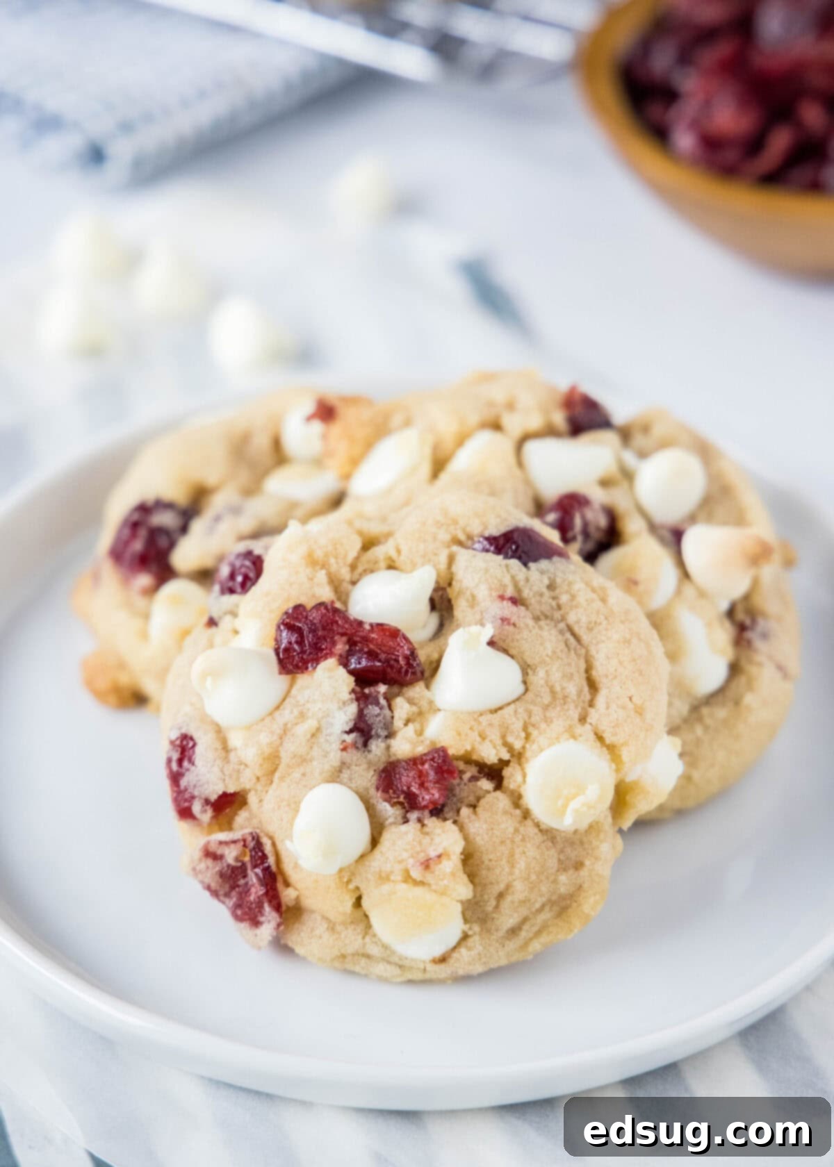 White chocolate cranberry cookies have crisp edges and soft, gooey centers, with tangy fruit, sweet white chocolate, and almond extract. Close up of three white chocolate cranberry cookies on a plate