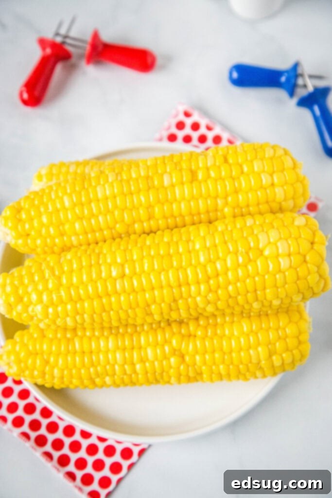 Easy Instant Pot Corn on the Cob 3 Fresh corn on the cob stacked on a white plate with a red and white napkin, ready to be cooked or served.