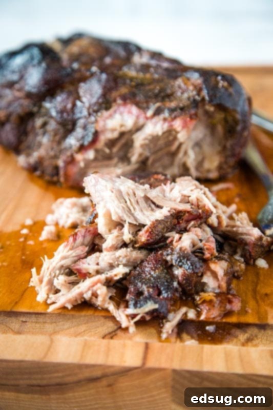 Smoked pork butt on cutting board with pile of pulled pork out front