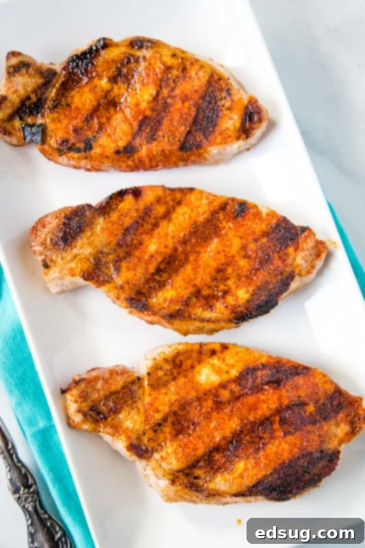 Sizzling Pork Chops 4 Freshly grilled pork chops resting on a white plate after being cooked to perfection, showcasing their enticing char and tenderness.