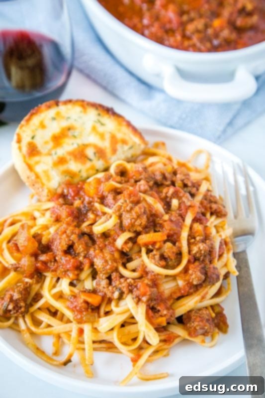 Quick Instant Pot Bolognese 3 Close-up of pasta with Instant Pot Bolognese sauce on a white plate, garnished with fresh herbs.