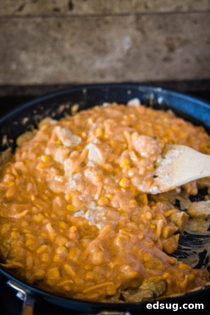 Enchilada Pasta Bake 4 adding corn and cheese sauce to the cooked chicken in a skillet