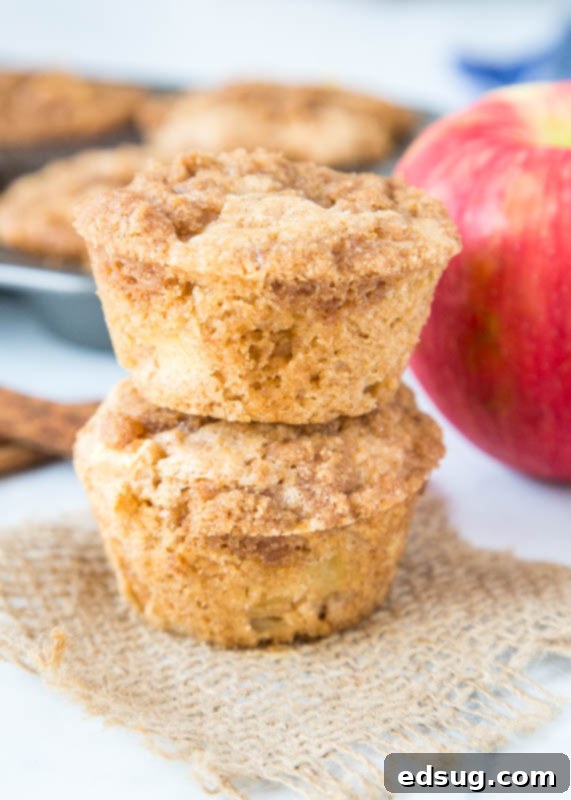 Warm Apple Cinnamon Muffins 5 Stacked apple muffins with a whole apple and cinnamon sticks on the side
