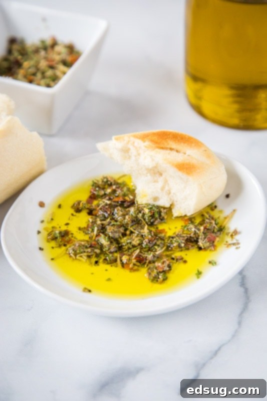 A close-up shot of Carrabba's-style bread dipping oil in a shallow white bowl, showing the rich green olive oil infused with specks of red pepper, dried herbs, and minced garlic.