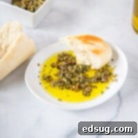 Close-up of a rustic bowl of bread dipping oil, featuring golden olive oil and a generous sprinkle of herbs, with a piece of artisanal bread on the side.