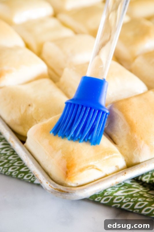 Freshly baked Texas Roadhouse rolls being brushed with melted butter for a glossy finish