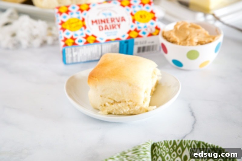 A warm Texas Roadhouse roll on a white plate with a small bowl of cinnamon honey butter beside it