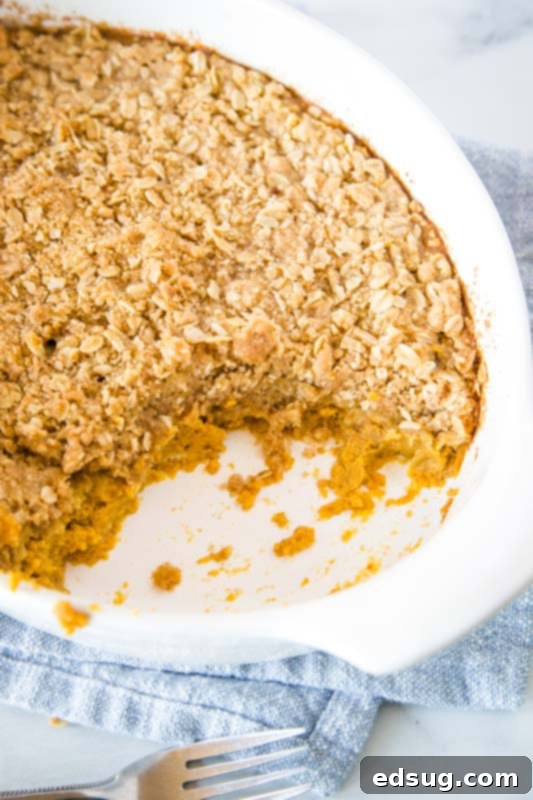 Pumpkin crisp in a rustic casserole dish with a piece removed, revealing the creamy pumpkin layer and golden brown streusel.